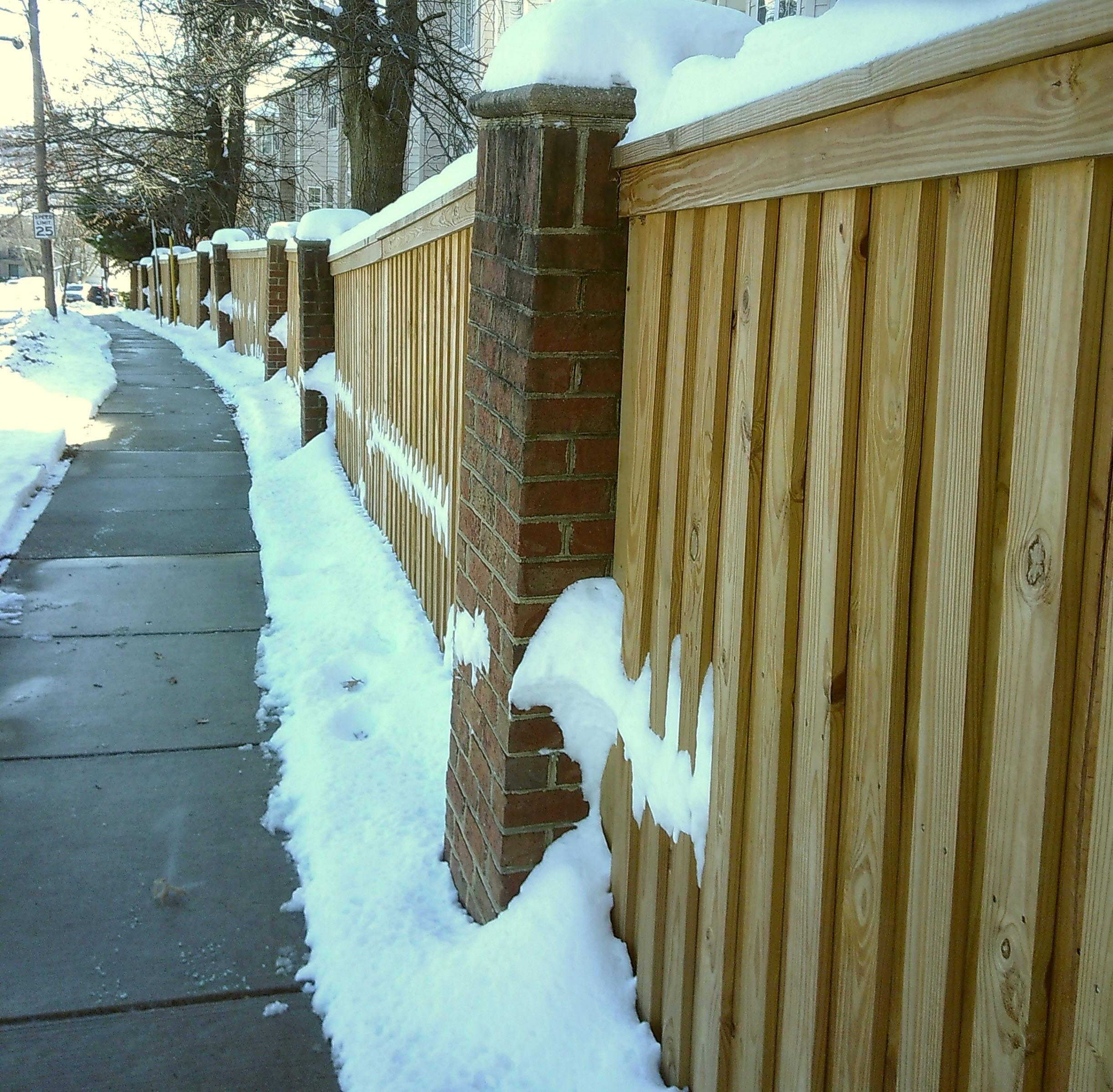 Snow surrounding a clear sidewalk along a fence