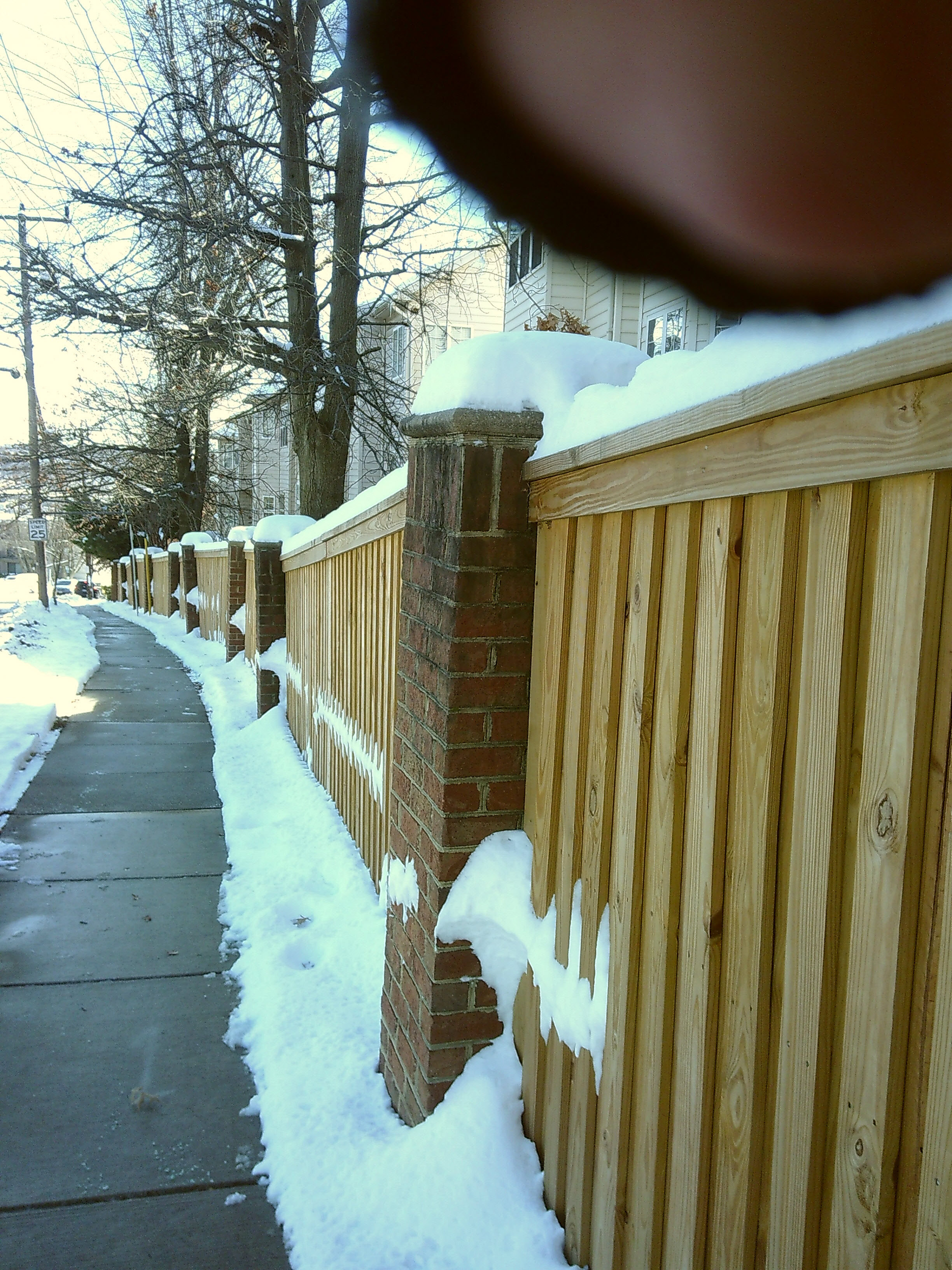 Snow surrounding a clear sidewalk along a fence with my finger on the top