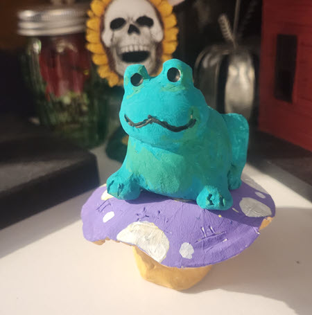 Handmade green frog sitting on top of a purple and yellow mushroom