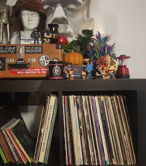 The top portion of an IKEA Kallax shelf showing 1 1/2 cubes containing records. On top sits various figurines from Monster Hunter, a phrenology head wearing an aviator hat, a suitcase covered in stickers, and Boris Karloff as Frankenstein looming behind on a wall poster