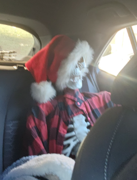 A skeleton with a Santa hat sits in the backseat of a car